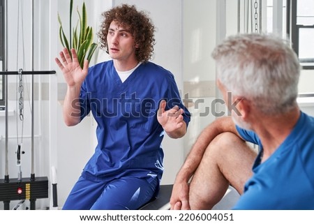 Skilful physical therapist giving instructions while chatting with his retirement client
