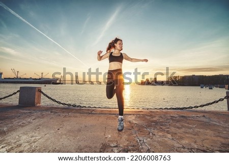 Young happy athletic looking woman jumping up against sea and sunset sky. Happy woman, photo in the air at the moment of the jump Royalty-Free Stock Photo #2206008763