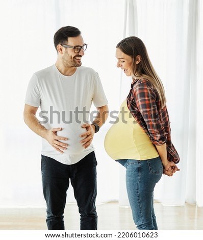 Happy young couple bonding, pregnent woman, father having fun both holding stomach at home Royalty-Free Stock Photo #2206010623