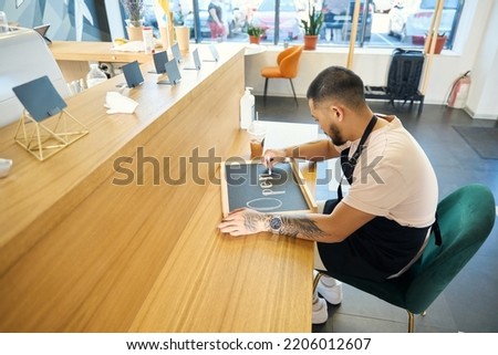 Enthusiastic young man preparing a chalkboard sign in his cafe