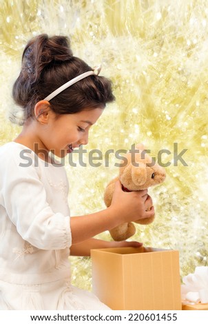 holidays, presents, christmas, childhood and people concept - smiling little girl with gift box over yellow lights background