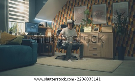 Man playing video game using modern VR headset and wireless controllers in leisure time in his room. Virtual reality device. Cyberspace and metaverse Royalty-Free Stock Photo #2206033141
