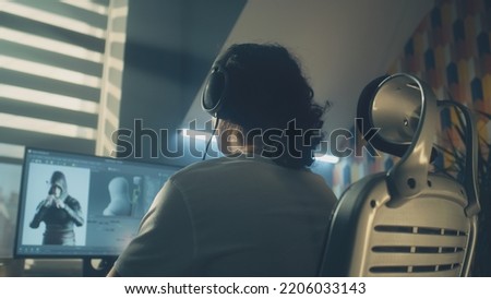 Man in headphones creating video game character in 3D modeling program while sitting at the table at home and working remotely on computer. Freelance. Game development