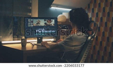 Male editor in headphones sitting at the table at night and editing video with astronauts for customer on pc in professional program while working remotely