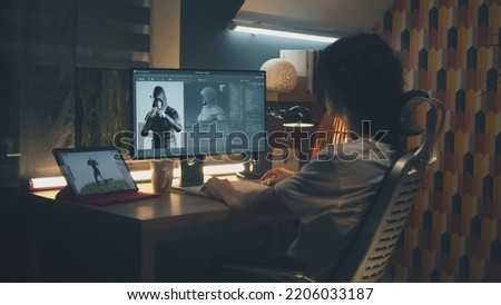 Male 3D designer sitting at the table at home and making animation for video game character, using modern computer and software for creating 3D modeling projects Royalty-Free Stock Photo #2206033187