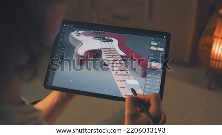 Man working at home remotely and creating 3D prototype of guitar in professional program using digital tablet computer and stylus