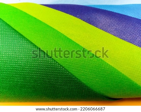 Bandung, Sept 24, 2022 : Texture of colorful nylon fabric shopping bags that rolling regular arranged with yellow plastic and light blue fabrics as background.