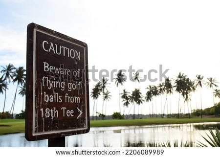 Caution sign board at the edge of 18th tee of golf course coconut palm trees cloudy white sky lake at the background in the dawn