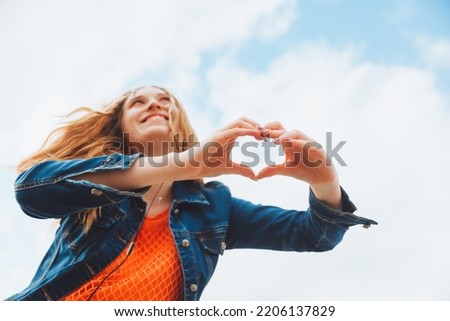 A young teenage girl holding hands in a heart-shaped frame against the sky