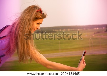 Beautiful young girl takes a selfie in the mountains at sunset. Young stylish fit slim woman travel blogger take photo selfie in traveling on mobile phone