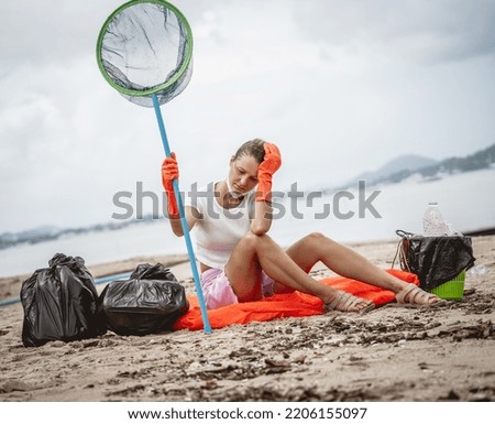 A female ecologist volunteer is resting after cleaning the beach on the seashore from plastic and other waste