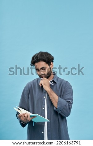 Thoughtful young arab buisness man or student holding notebook writing down notes making checklist, to do list, managing tasks and ideas standing isolated on blue background. Vertical