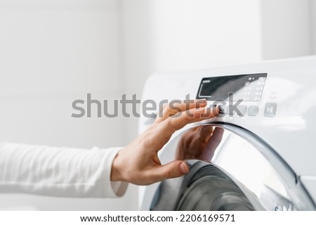 cropped shot of woman hand turn on automatic washing machine or select program with button on control panel in white bathroom in modern house Royalty-Free Stock Photo #2206169571