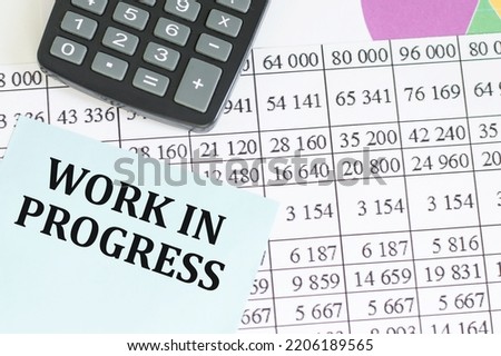 WORK IN PROGRESS inscription on a blue card on the background of financial reports on the table