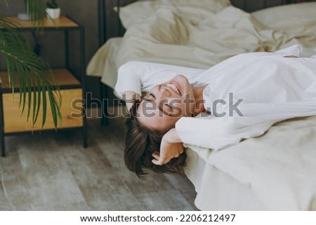 Side view calm fun young woman wear white shirt pajama she lying in bed close eyes rest relax spend time in bedroom lounge home in own room hotel wake up dream in good mood day Real estate concept. Royalty-Free Stock Photo #2206212497