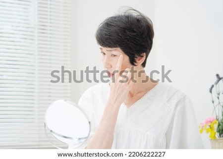 Asian middle aged woman looking in the mirror at home Royalty-Free Stock Photo #2206222227