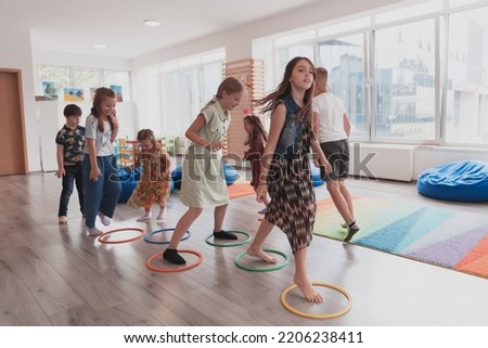 Small nursery school children with female teacher on floor indoors in classroom, doing exercise. Jumping over hula hoop circles track on the floor. Royalty-Free Stock Photo #2206238411