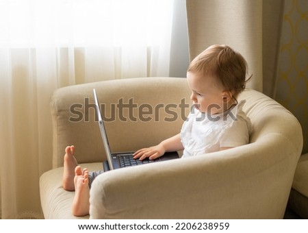 A baby in a light chair sits at a laptop and spoils his eyesight, watching cartoons