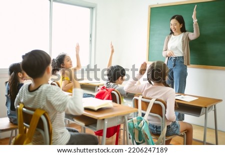 Group of Multi-ethnic happy elementary school children raising their arms to answer asian teacher question in classroom. Education, elementary school, learning, Back to school concept Royalty-Free Stock Photo #2206247189