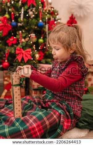 The child opens a gift near the Christmas tree. Happy Holidays. A cute little child with surprise on his face opens a gift near the Christmas tree.