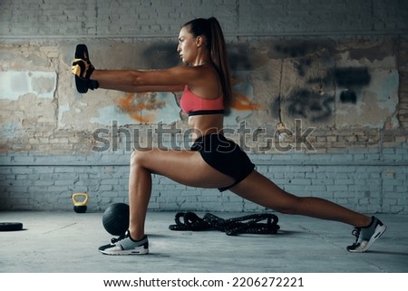 Full length of beautiful young woman doing weight training in gym 