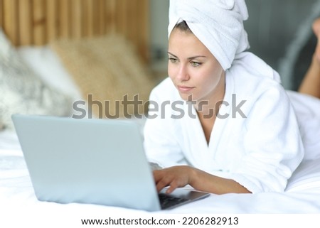 Beautiful woman lying on a bed after showering using laptop at home