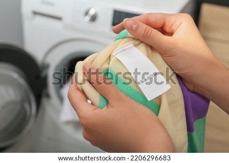 Woman holding apparel with blank clothing label at home, closeup
