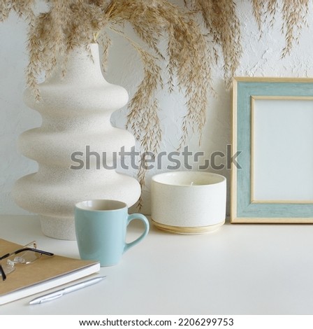 Modern women's home office workspace with photo frame mockup.  Aesthetic scandy hygge style.Cup coffee, photo frame,planner, vase with grass,aroma candle .Copy space.Neutral colors home design.