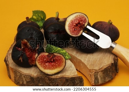 Dark figs on a wooden board on an orange background. Shallow depth of field