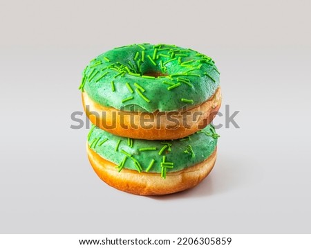 Two doughnuts, covered with green icing with green sprinkles, lie on top of each other on a white background