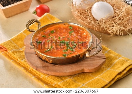 Famous Turkish name menemen in traditional copper pan on the beige table.  Menemen made by eggs, pepper and tomatoes. Traditional Turkish food Menemen concept for menu. Royalty-Free Stock Photo #2206307667