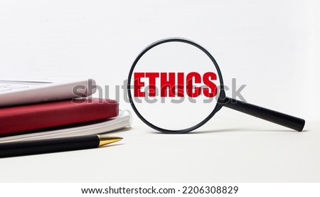 Office table with notepads, black calculator, pen and magnifying glass with ETHICS inscription. Side view.