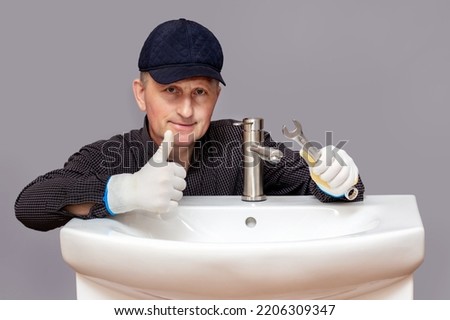 Satisfied with the work, the plumber near the sink with the installed faucet shows the ok sign with his hand