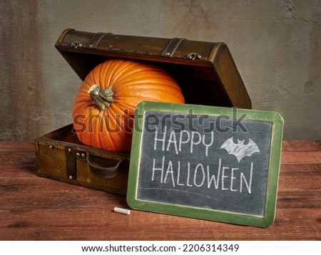 Happy Halloween blackboard sign with a large pumpkin in a small retro suitcase, greeting card