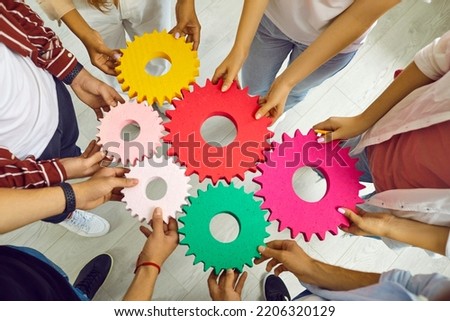 Team of people connecting gears. Cropped shot group of young men and women standing in circle and joining colorful cogs together. Teamwork, integration, business, education, success concept background Royalty-Free Stock Photo #2206320129