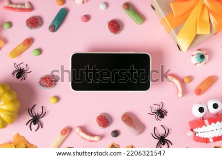 A smartphone with a black blank screen on a pink background with creepy marmalades. A banner for the Halloween holiday. Copy space. Flat lay, top view.