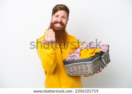 Redhead man with beard holding a clothes basket isolated on white background inviting to come with hand. Happy that you came