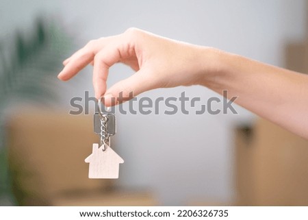 Female Hand Holding House Keys Inside Empty Room with Boxes Banner. Real estate agent handing over house keys in hand. Close-up view of keys from new home on cardboard box during relocation. Royalty-Free Stock Photo #2206326735