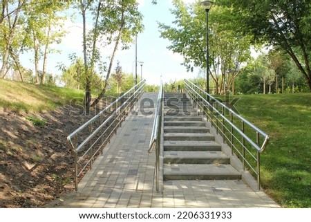 Stairs and ramp with metal railings for the passage of strollers and wheelchairs in public park. Concept of comfortable barrier-free urban environment in city. Pathway for people with disabilities Royalty-Free Stock Photo #2206331933