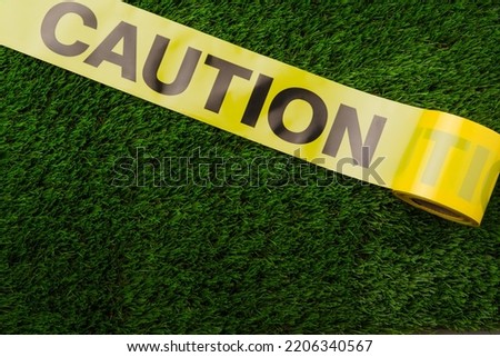 Close-up. Yellow plastic tape with the inscription CAUTION on a green lawn. Barrier, fencing, danger warning and traffic restriction. Crime scene, quarantine, facilities under construction.