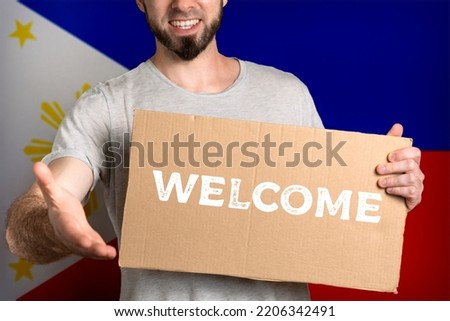 The concept of tolerance for immigrants and people of different life positions. A man holds a cardboard and stretches out his hand to greet. Flag of Philippines. Text welcome.