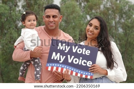 A young smiling Hispanic family holds up a voting sign reading "My Vote My Voice"                                 