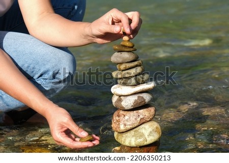 Close-up of a woman's hand laying the last stone on the gravel by the stream on a sunny day, copy space. Concept of balance, harmony.