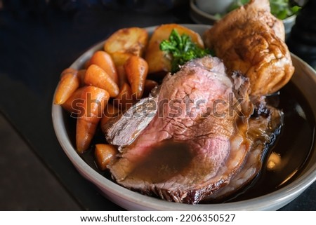 Roast beef slices on a plate with carrots, roast potatoes, a Yorkshire pudding and gravy, making a complete Sunday roast meal.  Royalty-Free Stock Photo #2206350527