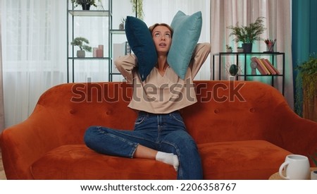 Repair work at neighbours concept. Irritated woman sit on couch cover ears with pillows annoyed by noisy neighbors suffer from headache wishes silence. Thin walls at home flat without sound insulation Royalty-Free Stock Photo #2206358767