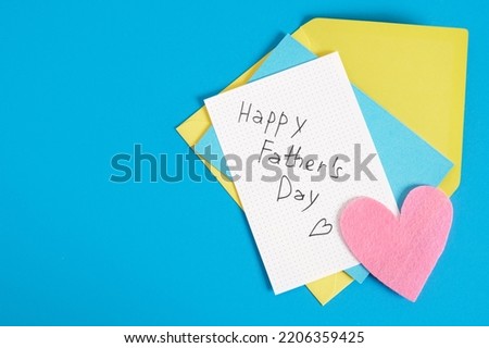 lettering happy father's day on paper, felt heart, postcard and envelope on blue background top view copy space