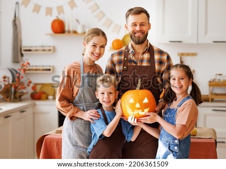 Happy family mother, father and children smiling  at camera make jack-o-lantern from pumpkin during   celebration, getting ready for halloween
