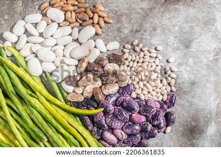 Different varieties of beans on a gray background. Top view, copy space. Harvest and vegetarianism concept. 