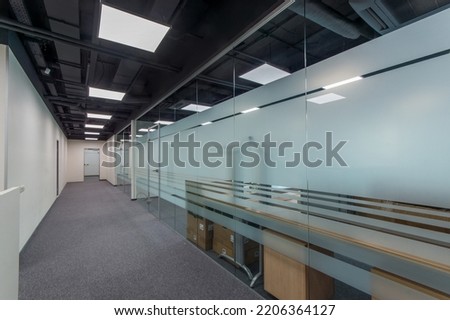 A wide corridor of a modern office with furniture behind glass partitions. Royalty-Free Stock Photo #2206364127