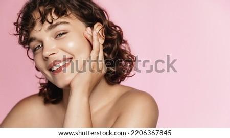 Beautiful curly girl smiles as she likes skincare effect after beauty gel. Portrait of young woman washing her face and body, pink background. Royalty-Free Stock Photo #2206367845